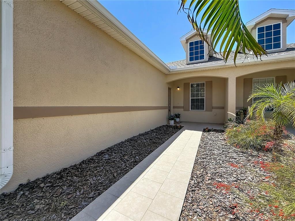A beige house exterior features a two-car garage, a concrete driveway, and surrounding landscaping — 1027 ORCA COURT, HOLIDAY, FL