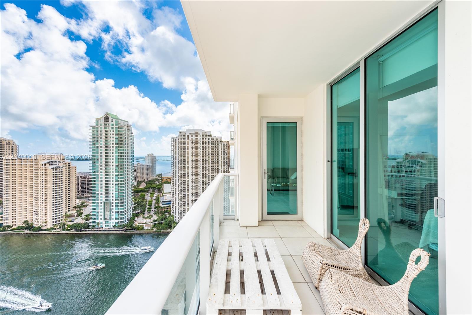A high-rise balcony features a white slatted bench, two woven chairs, and a water view — 300 S Biscayne Blvd # 2814, Miami FL 33131, MIAMI, FL