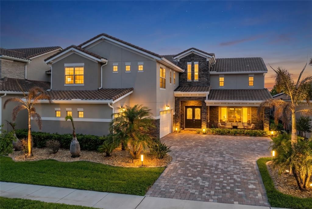 A two-story house with a stone facade, tile roof, and a paved driveway at dusk — 13352 ALDERLEY DRIVE, ORLANDO, FL