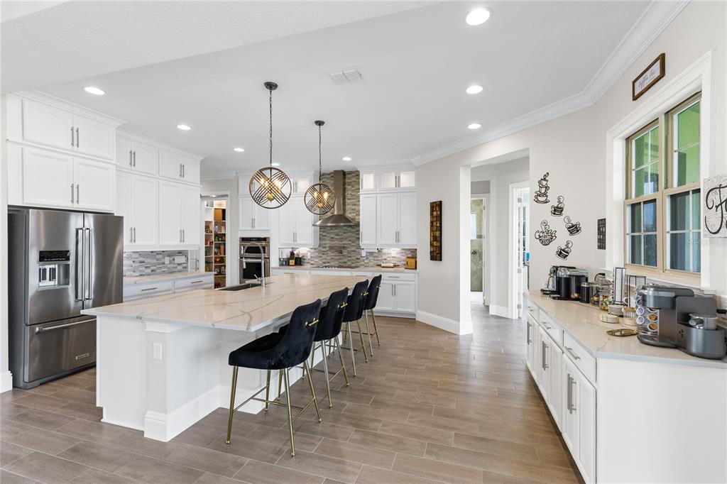 A modern white kitchen features a large quartz island, black bar stools, and stainless appliances — 13352 ALDERLEY DRIVE, ORLANDO, FL