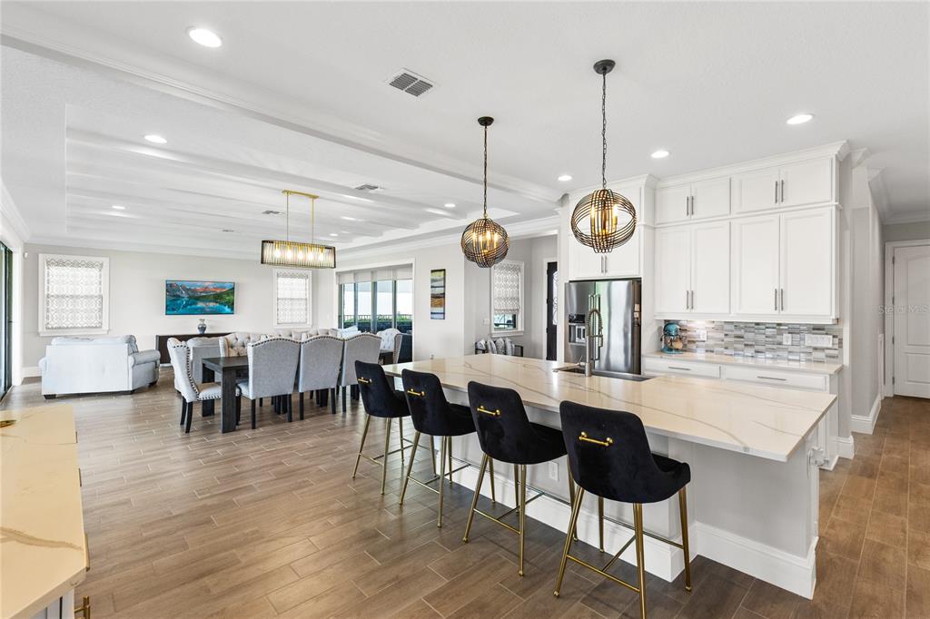A modern open-concept kitchen and dining area features white cabinetry, a large island, and tile flooring — 13352 ALDERLEY DRIVE, ORLANDO, FL
