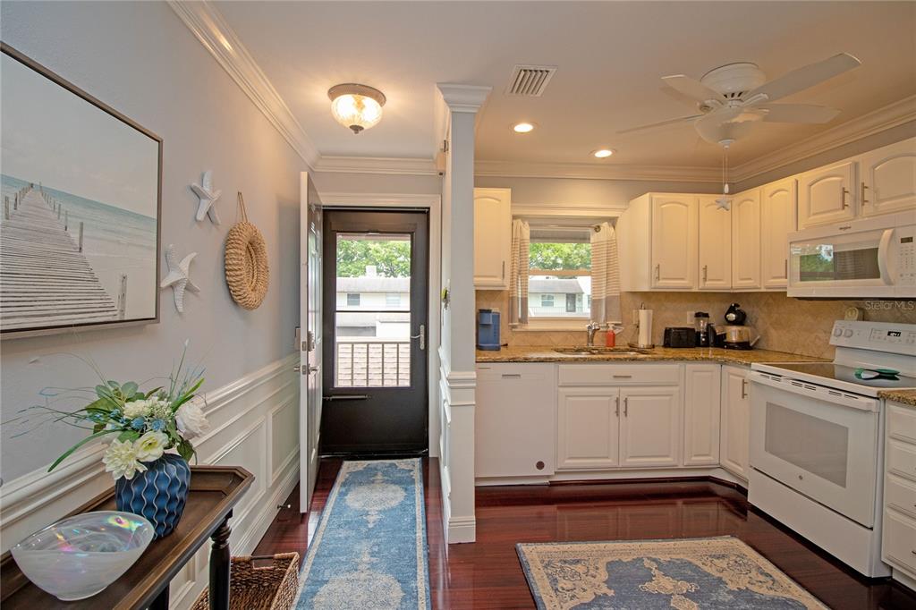 A kitchen with white cabinets and granite countertops sits next to an entryway with hardwood floors — 1100 E BAY DRIVE UNIT 104, LARGO, FL