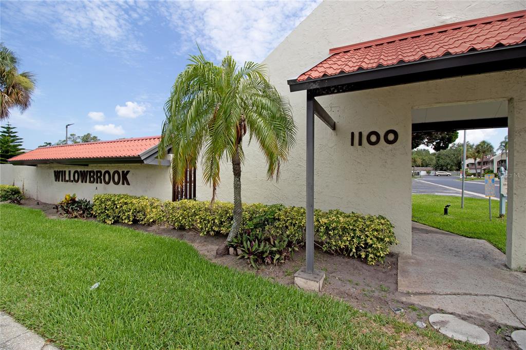 The exterior of a building features a red tile roof, a palm tree, and landscaping — 1100 E BAY DRIVE UNIT 104, LARGO, FL
