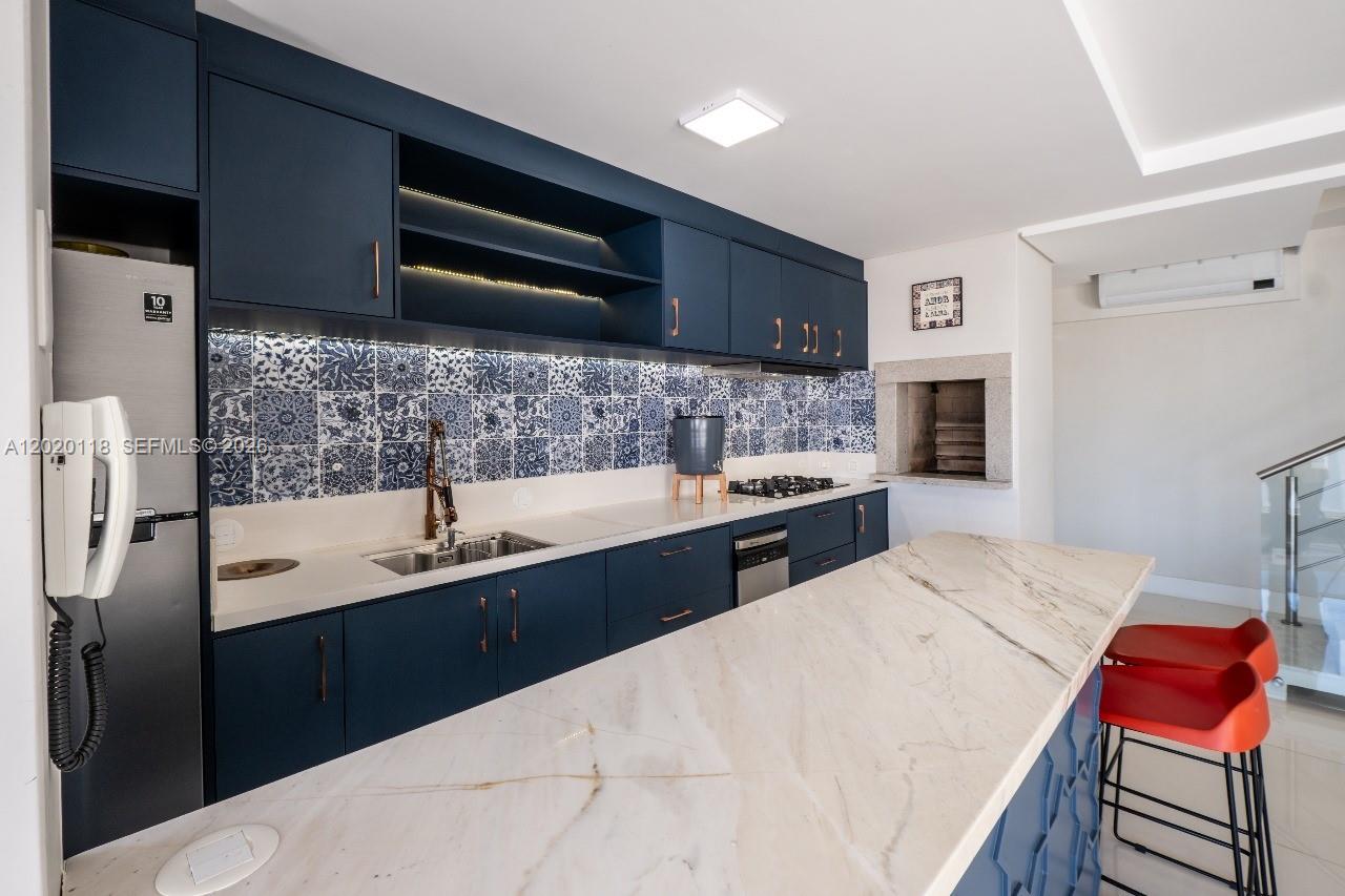 A modern kitchen features dark blue cabinets, patterned blue tile backsplash, and a marble island — 1540 Rua das Piraunas # 403, SC 88053418, SC