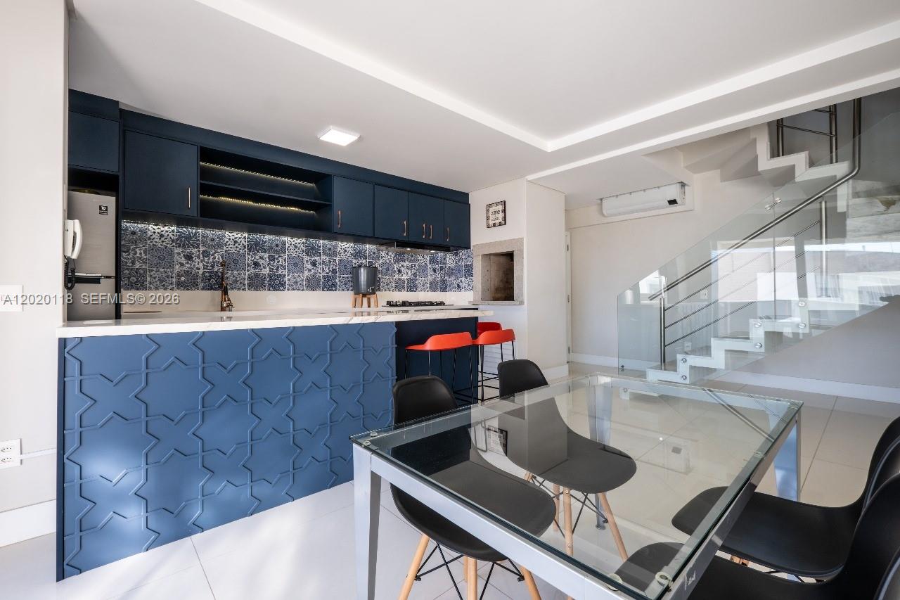 A modern kitchen features dark blue cabinetry, a patterned backsplash, and an adjacent glass dining table — 1540 Rua das Piraunas # 403, SC 88053418, SC
