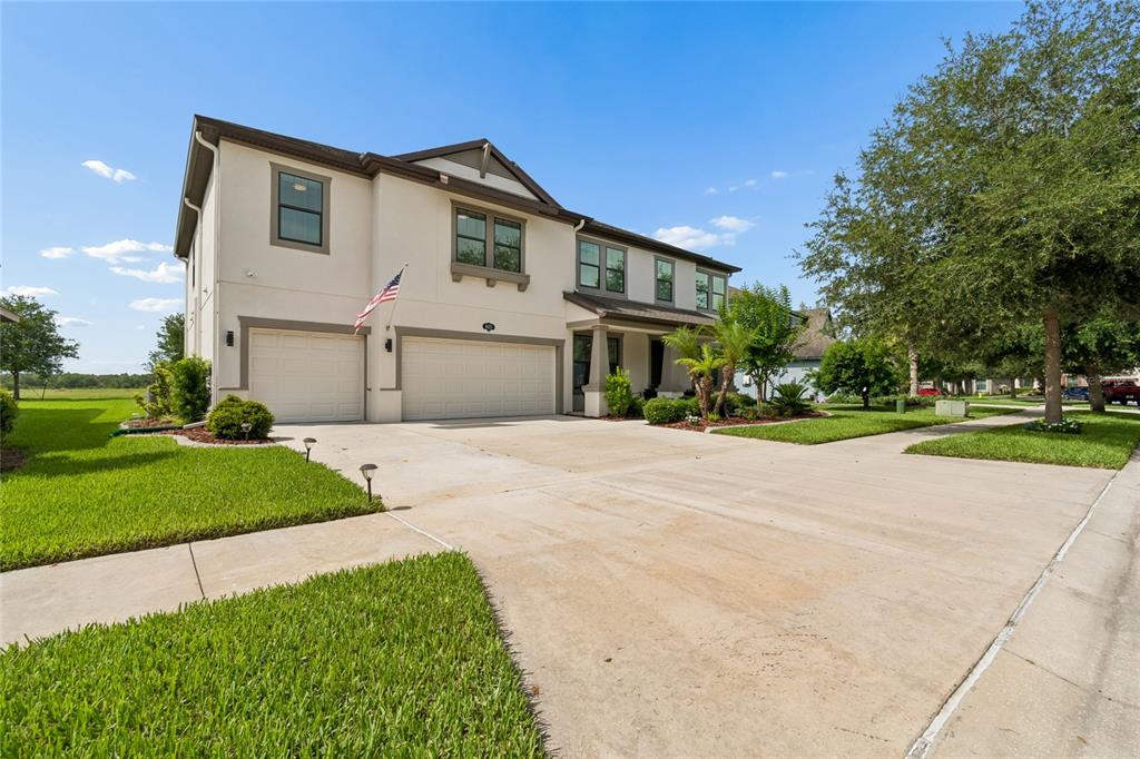 A two-story house with a three-car garage and a concrete driveway under a blue sky — 10623 MISTFLOWER LANE, TAMPA, FL