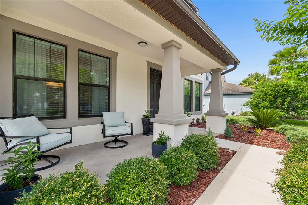 A covered front porch features a herringbone paver floor, two chairs, and tapered support columns — 10623 MISTFLOWER LANE, TAMPA, FL