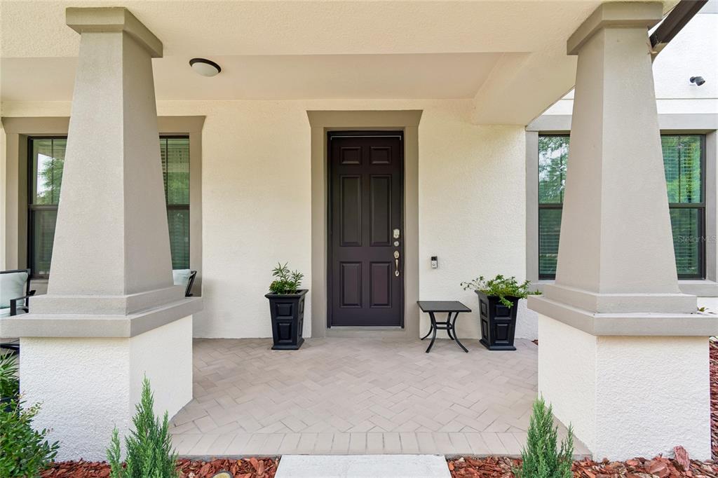 A covered front porch features a dark door, two large pillars, and herringbone-patterned pavers — 10623 MISTFLOWER LANE, TAMPA, FL