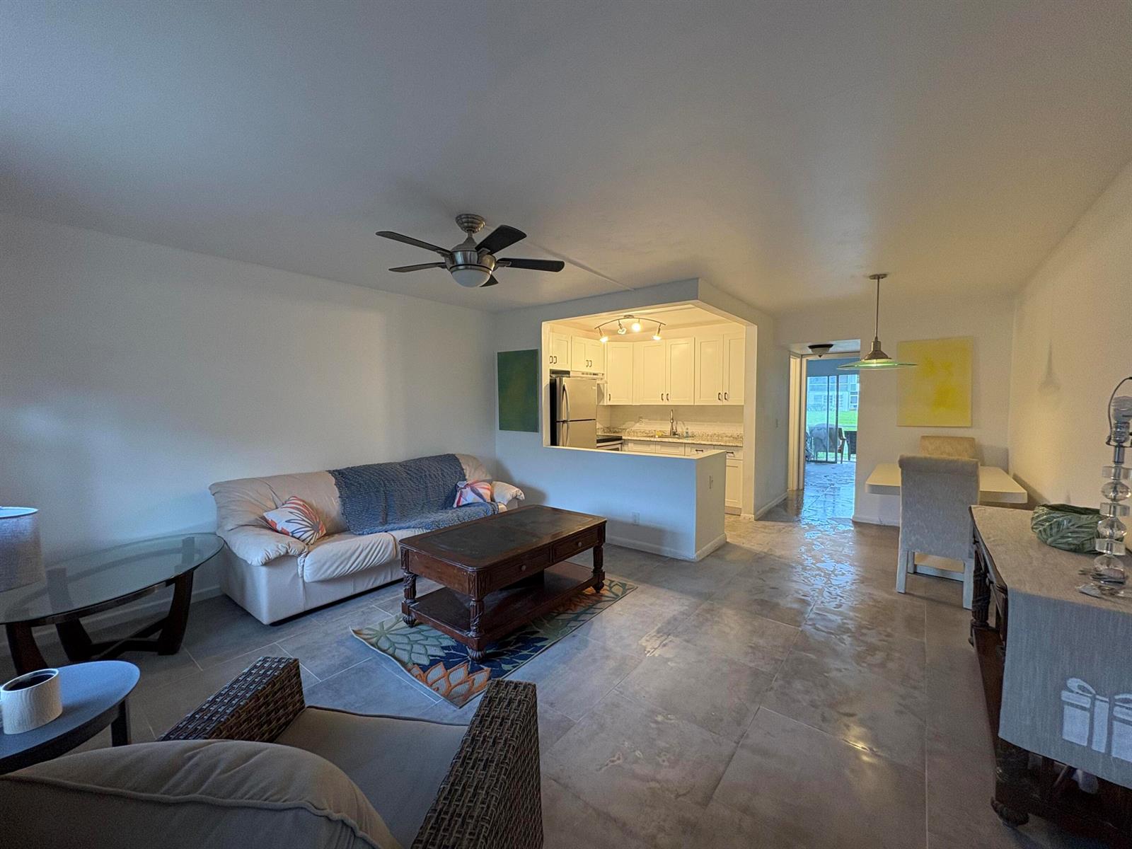 An open-concept living and dining area features tile flooring, a kitchen pass-through, and ceiling fans — 2 Kent A, West Palm Beach FL 33417, WEST PALM BEACH, FL