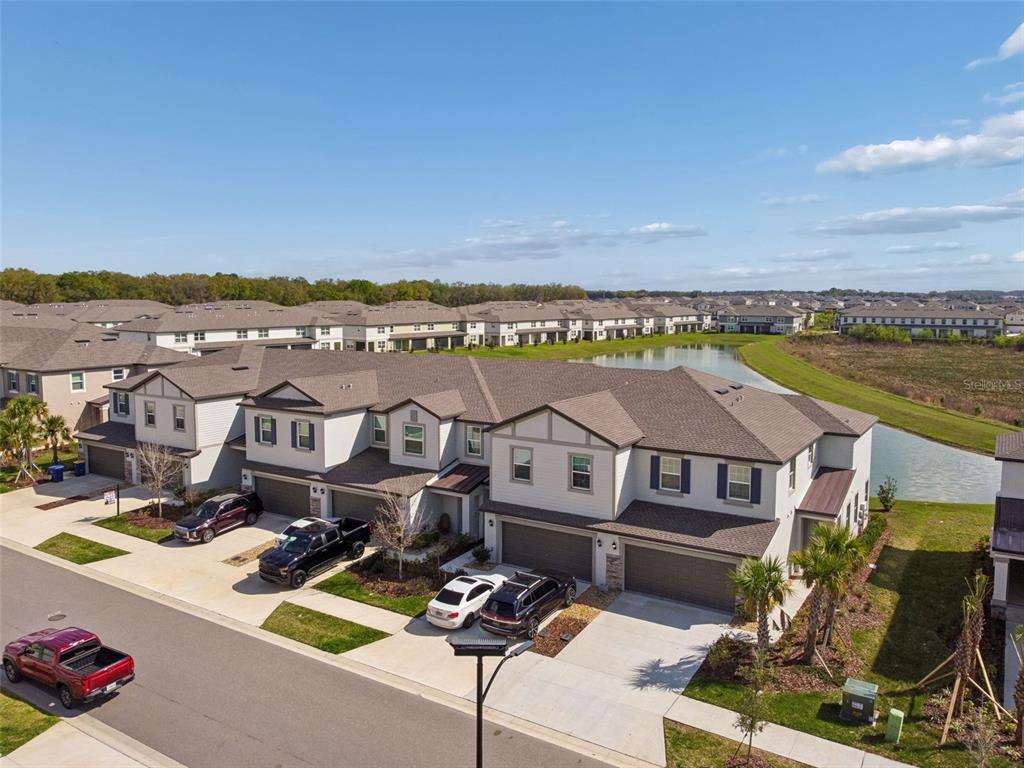 An aerial view of a multi-unit townhouse complex with attached garages and a nearby pond — 32076 POP ASH PLACE, SAN ANTONIO, FL