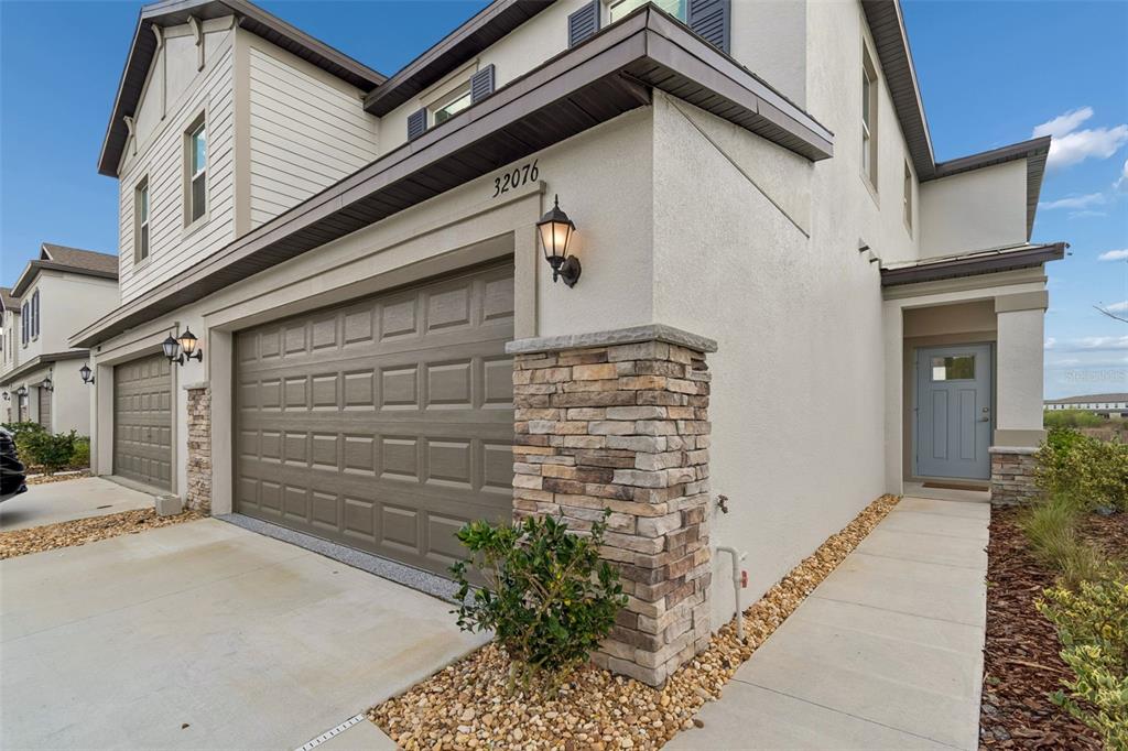 A two-story townhouse exterior features a tan stucco facade, stone accents, and a gray garage — 32076 POP ASH PLACE, SAN ANTONIO, FL