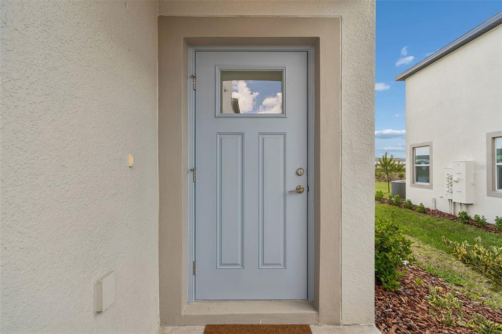 A light blue front door with a small window is set into a stucco exterior wall — 32076 POP ASH PLACE, SAN ANTONIO, FL