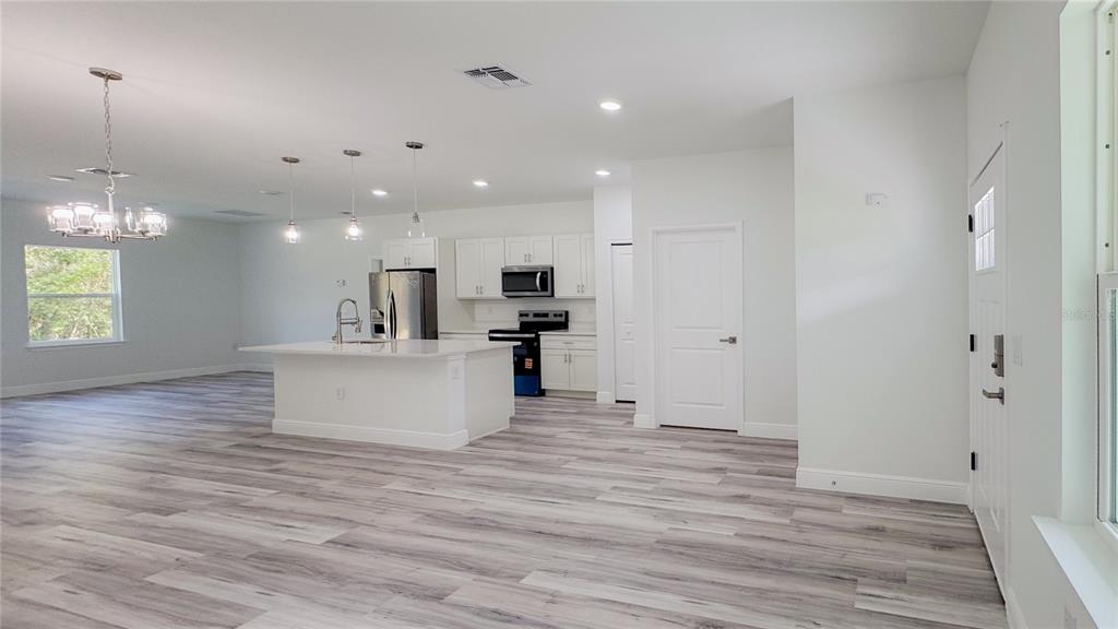 An open-concept kitchen features white cabinetry, a central island, and light wood-look flooring — 15625 SW 37TH CIRCLE, OCALA, FL