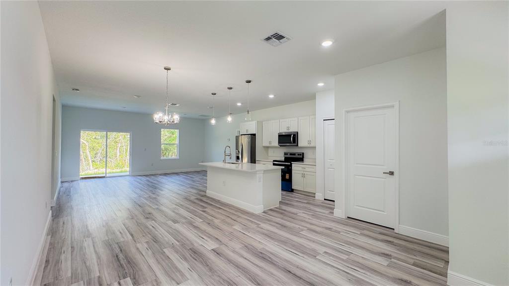 An open-concept kitchen and living area with white cabinets, a central island, and wood-look flooring — 15625 SW 37TH CIRCLE, OCALA, FL