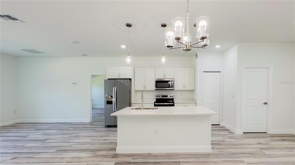 A modern kitchen features white cabinets, stainless steel appliances, a center island, and wood-look flooring — 15625 SW 37TH CIRCLE, OCALA, FL