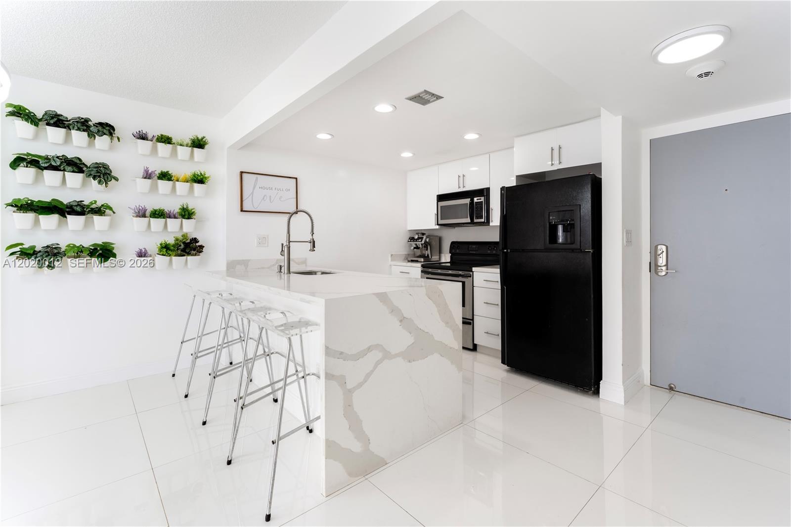 A modern kitchen features a white marble waterfall island, black appliances, and a vertical plant wall — 600 NE 36th St # 1111, Miami FL 33137, MIAMI, FL