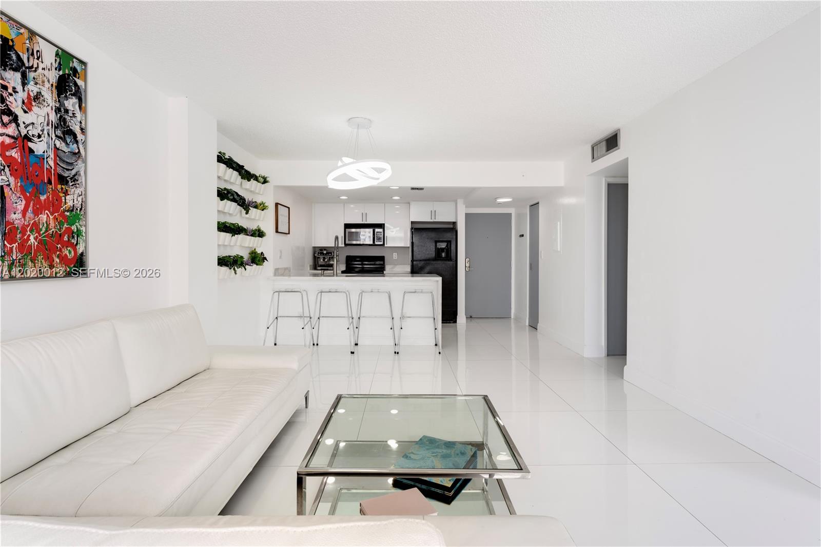 A modern living room features white tile floors, a white sofa, and an open kitchen — 600 NE 36th St # 1111, Miami FL 33137, MIAMI, FL