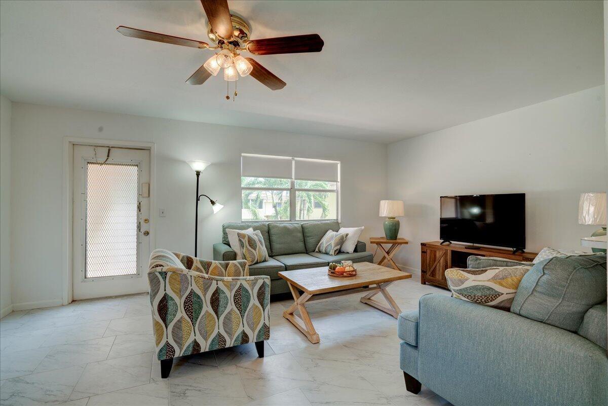 A living room features a blue sofa, patterned armchair, wood coffee table, and tile flooring — 222 Saxony E # 222, Delray Beach FL 33446, DELRAY BEACH, FL