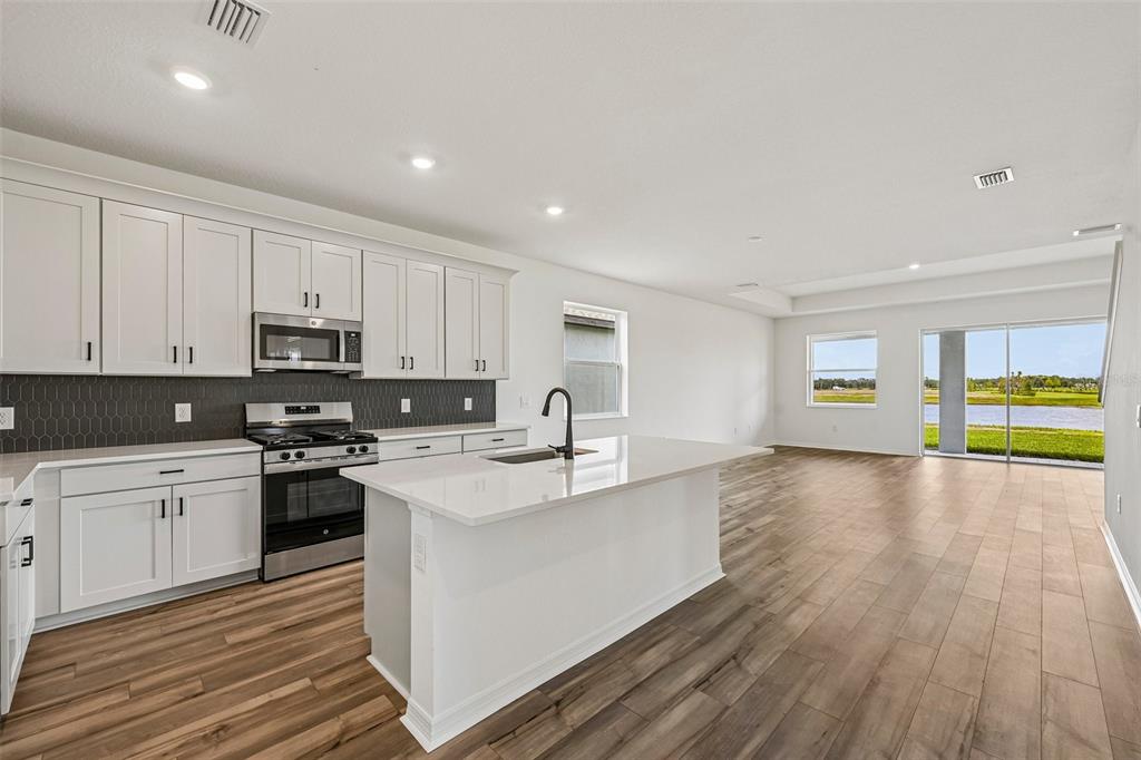 A modern kitchen with white cabinets, a central island, and wood-look flooring opens to living space — 8724 CANARD COVE, PALMETTO, FL