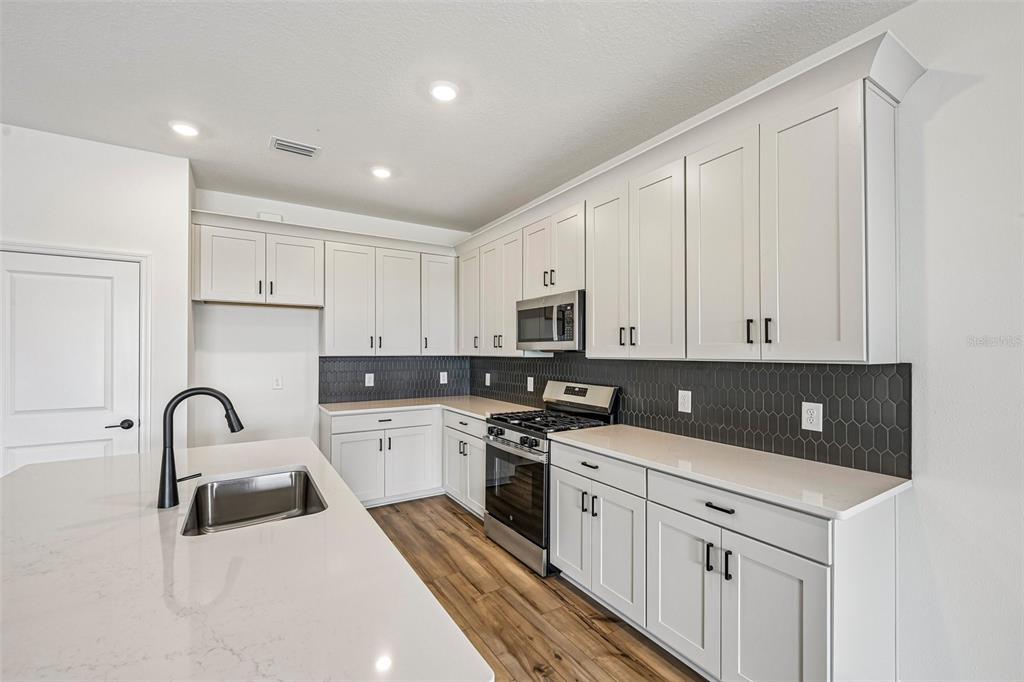 A modern kitchen features white cabinets, quartz countertops, a dark hexagonal tile backsplash, and stainless appliances — 8724 CANARD COVE, PALMETTO, FL