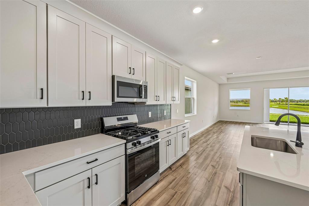A modern kitchen features white cabinets, stainless steel appliances, quartz countertops, and a dark backsplash — 8724 CANARD COVE, PALMETTO, FL