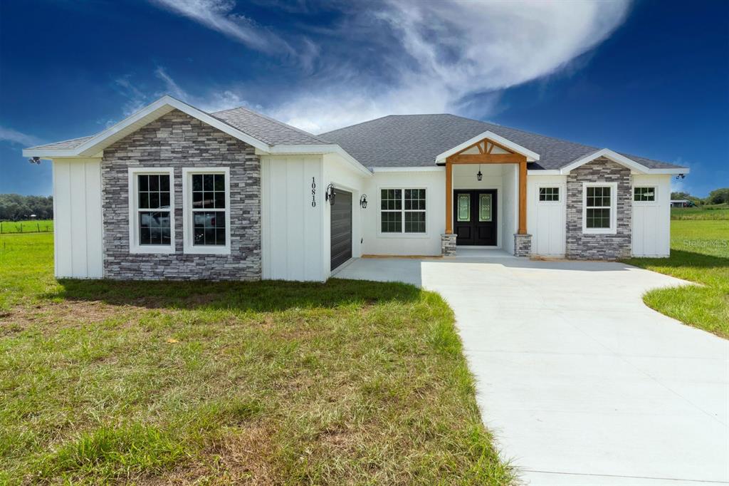 A single-story house features white vertical siding, stone veneer accents, and a concrete driveway — TBD LOT 01000 SILVER DRIVE, UMATILLA, FL