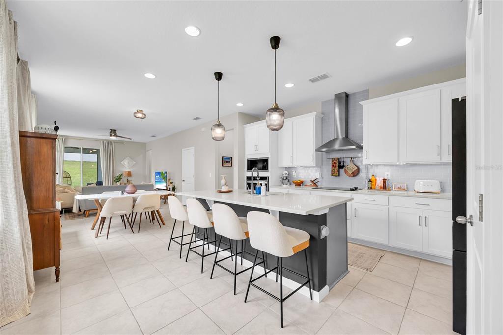 A modern kitchen with white cabinets, a gray island, and bar seating opens to a dining area — 4316 RENLY LANE, CLERMONT, FL