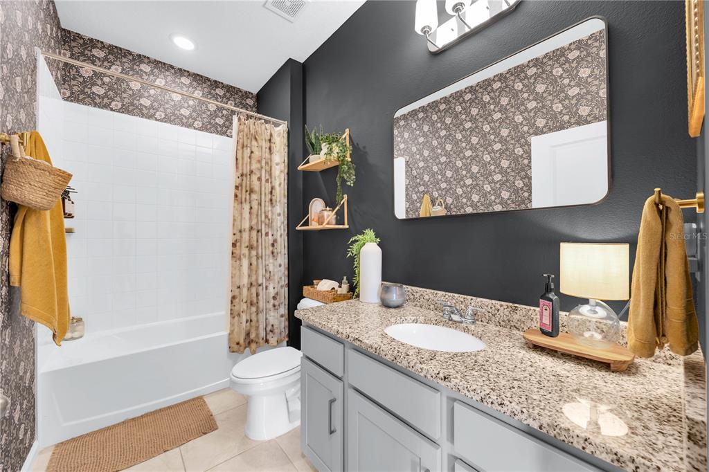 A bathroom features a granite vanity, dark walls, floral wallpaper, and a shower-tub combination — 4316 RENLY LANE, CLERMONT, FL
