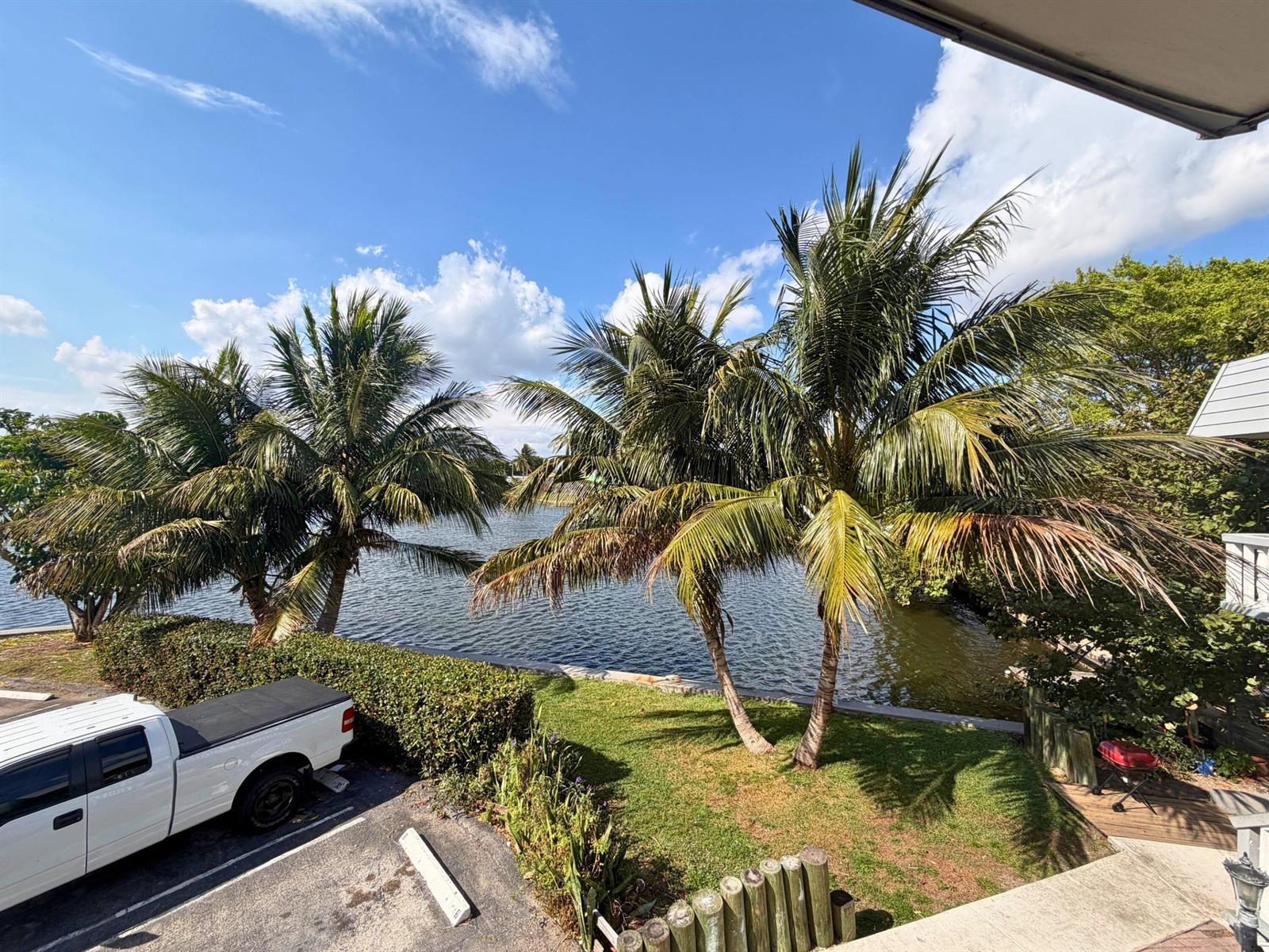 A view of a calm canal with a small dock and boat from a grassy bank — 519 W Kalmia Drive # 2, West Palm Beach FL 33403, WEST PALM BEACH, FL