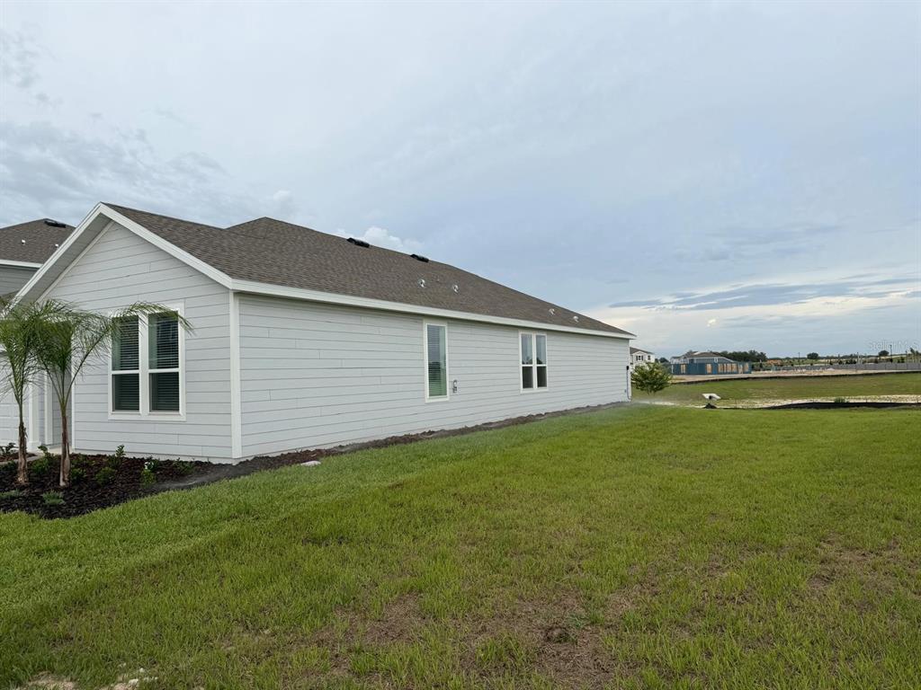 The side exterior of a light gray house with a shingled roof and green lawn — 2732 MERCY CIRCLE, CLERMONT, FL