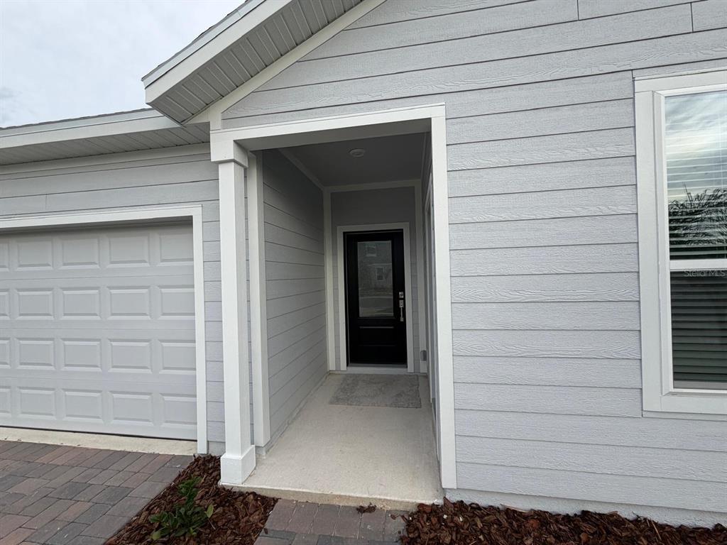 A light gray house exterior features a covered entryway with a black front door — 2732 MERCY CIRCLE, CLERMONT, FL