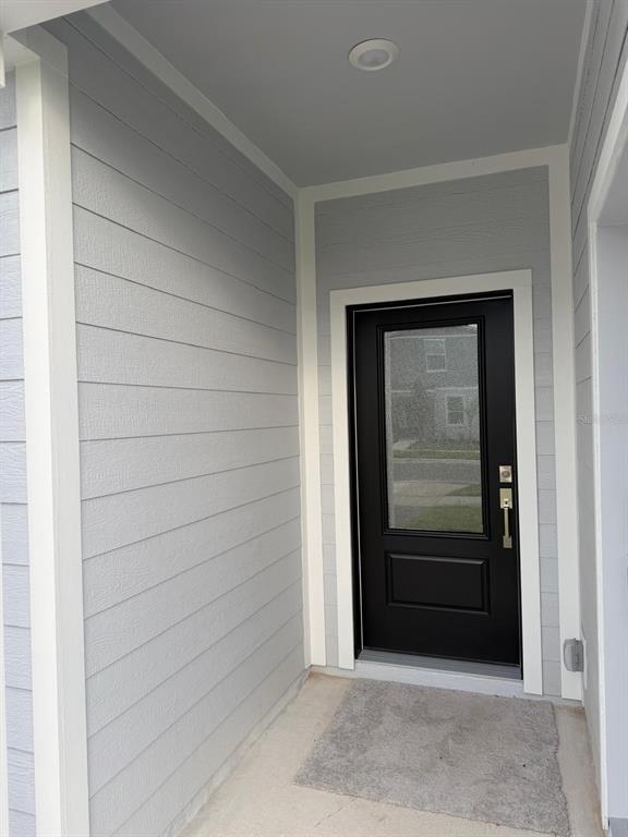 A covered entryway features light gray horizontal siding, a black front door, and concrete flooring — 2732 MERCY CIRCLE, CLERMONT, FL