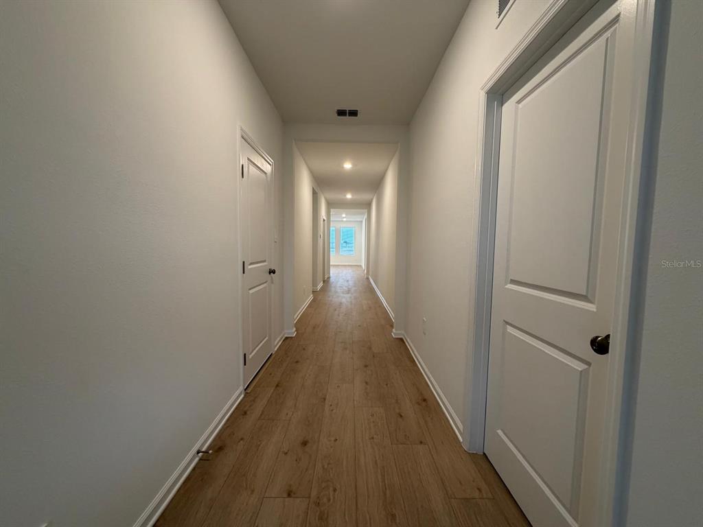 A long hallway with light wood-look flooring and white doors on both sides — 2732 MERCY CIRCLE, CLERMONT, FL