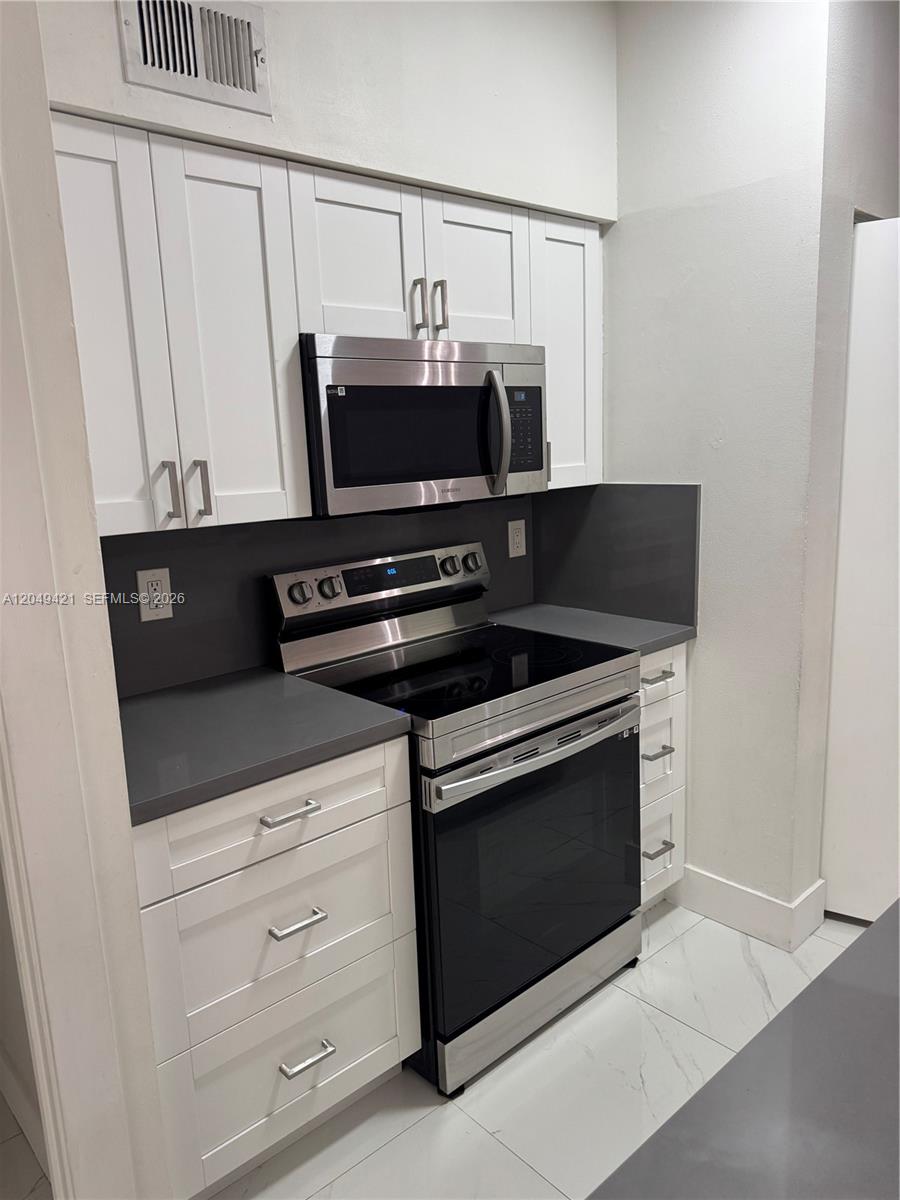 A kitchen features white cabinets, stainless steel appliances, and dark gray countertops — 18344 NW 68th Ave # F, Hialeah FL 33015, HIALEAH, FL