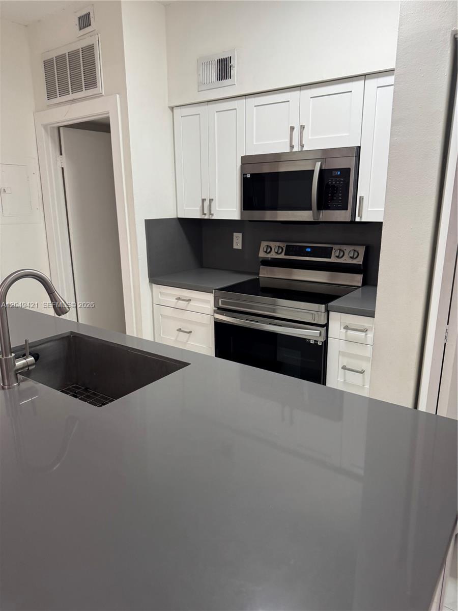 A kitchen features white cabinets, gray countertops, and stainless steel appliances — 18344 NW 68th Ave # F, Hialeah FL 33015, HIALEAH, FL