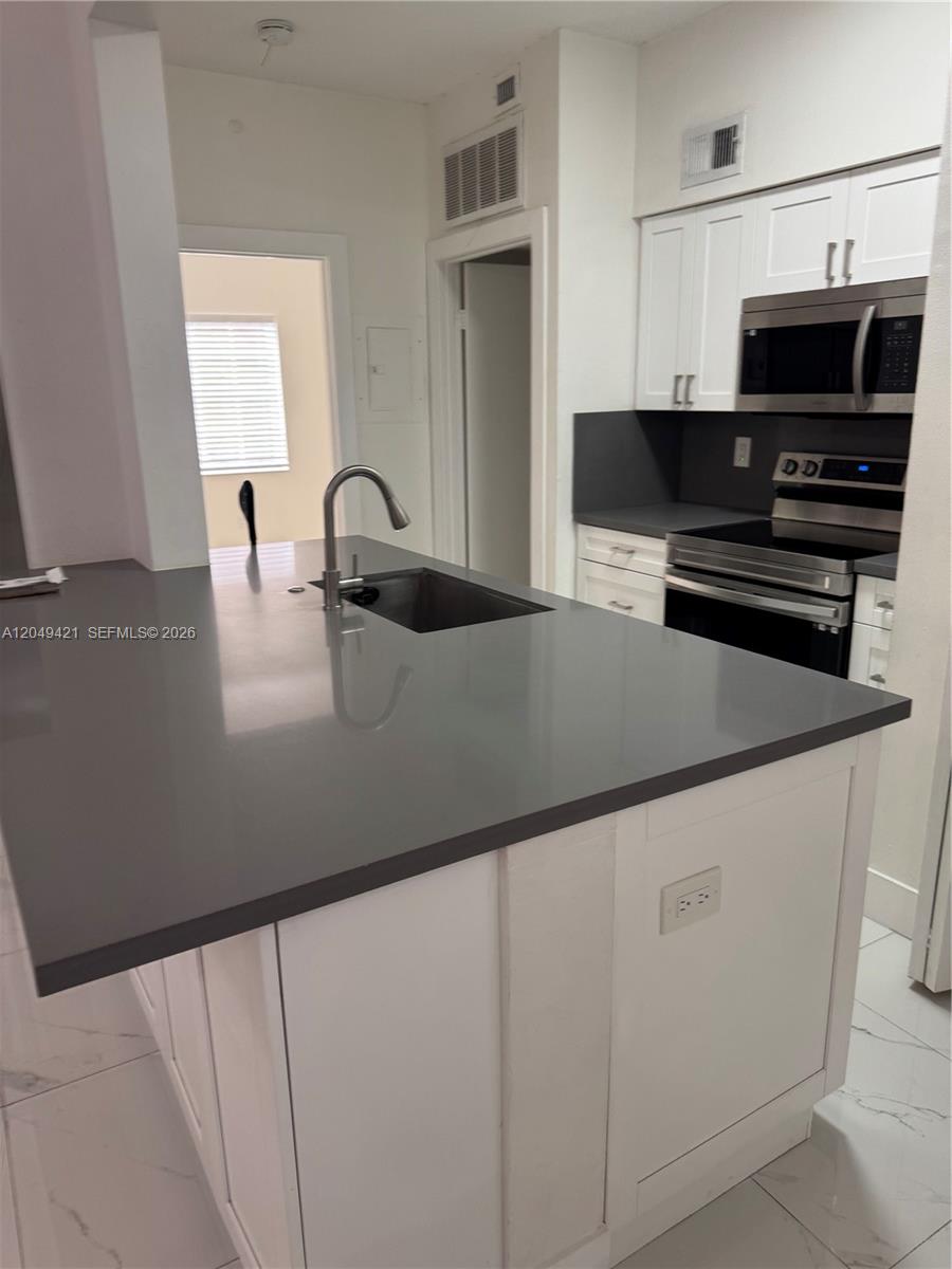 A kitchen features a gray quartz island with a sink, white cabinets, and stainless appliances — 18344 NW 68th Ave # F, Hialeah FL 33015, HIALEAH, FL