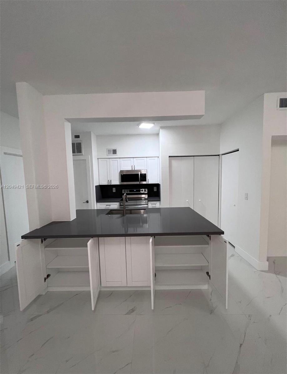 A kitchen features a dark countertop island with open cabinets, white cupboards, and light flooring — 18344 NW 68th Ave # F, Hialeah FL 33015, HIALEAH, FL