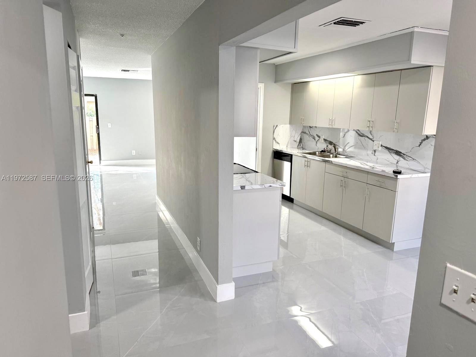 A modern kitchen features light gray cabinets, marble-patterned backsplash, and glossy white tile flooring — 2700 N 34th Ave # I, Hollywood FL 33021, HOLLYWOOD, FL