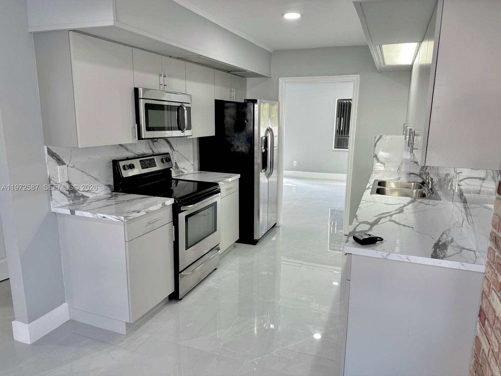 A modern galley kitchen features light gray cabinets, marble-patterned countertops, and stainless steel appliances — 2700 N 34th Ave # I, Hollywood FL 33021, HOLLYWOOD, FL