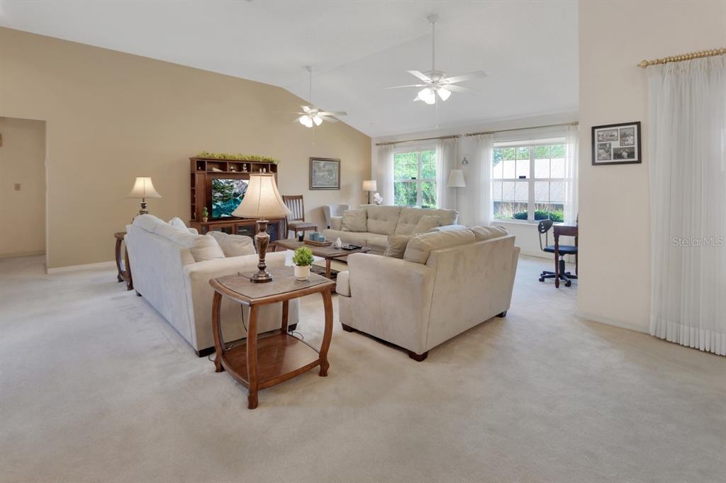 A spacious living room features beige carpeting, vaulted ceilings, two ceiling fans, and neutral furniture — 2520 S GLEN EAGLES DRIVE, DELAND, FL