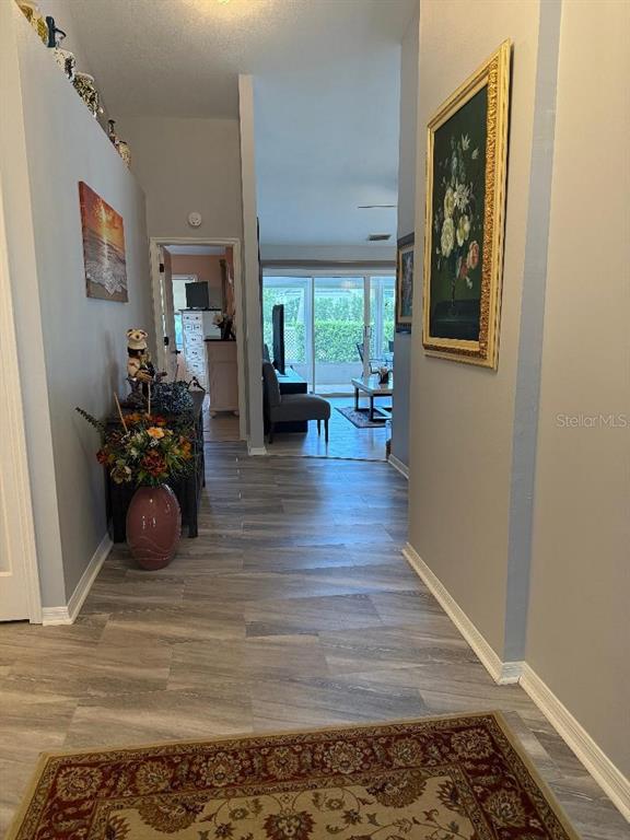 A hallway with wood-look flooring leads toward a living area with a glass sliding door — 4716 61ST AVENUE TERRACE W UNIT 4716, BRADENTON, FL