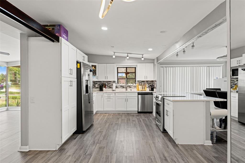A modern kitchen features white cabinets, stainless steel appliances, and gray wood-look flooring — 2116 W ABDELLA STREET, TAMPA, FL