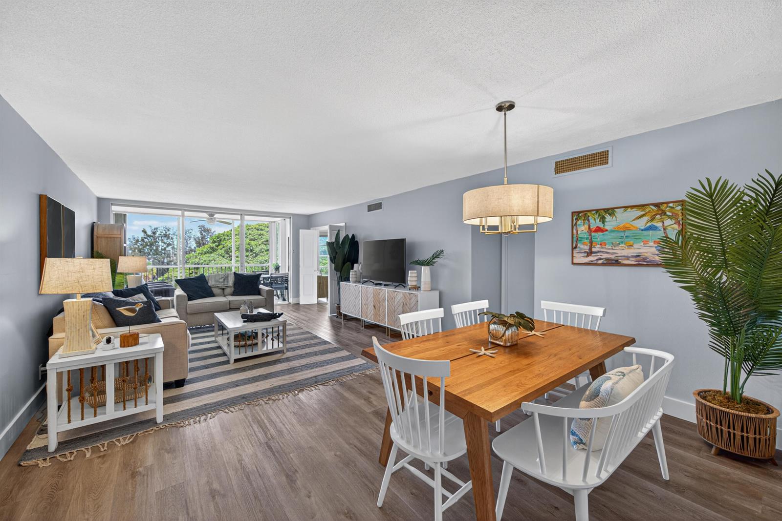 A living and dining room with light blue walls, wood-look flooring, and a balcony view — 2650 S Course Drive # 603, Pompano Beach FL 33069, POMPANO BEACH, FL