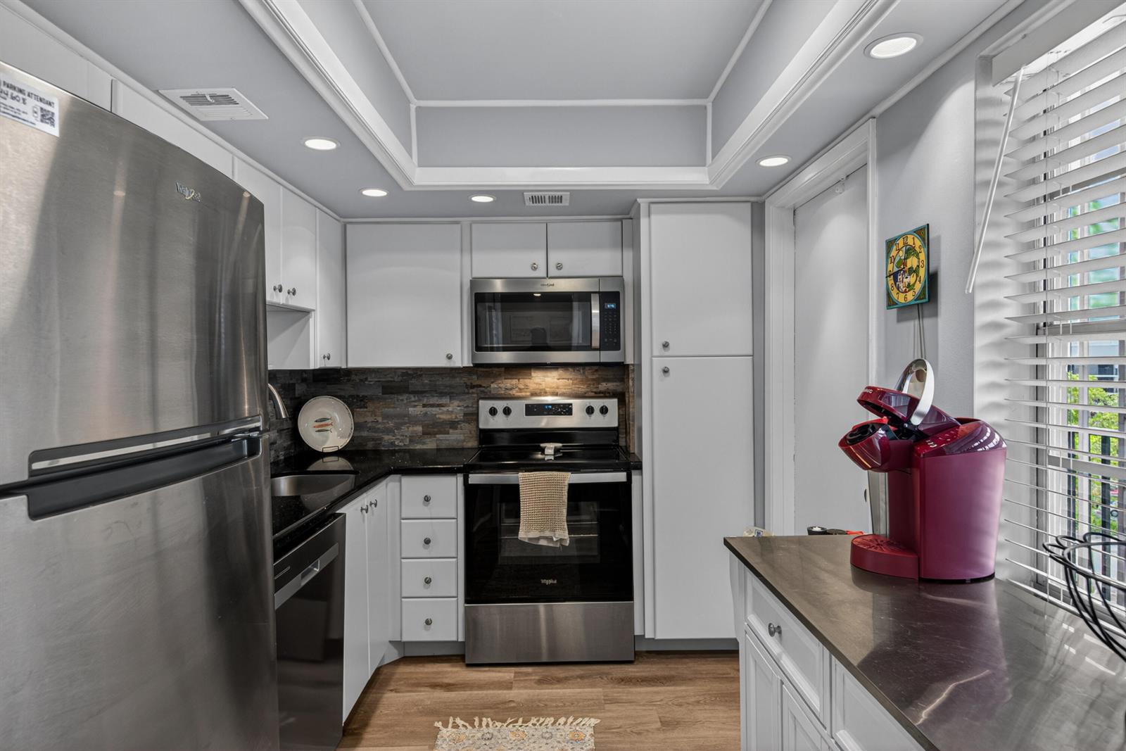 A kitchen features white cabinets, stainless steel appliances, a dark stone backsplash, and wood flooring — 2650 S Course Drive # 603, Pompano Beach FL 33069, POMPANO BEACH, FL