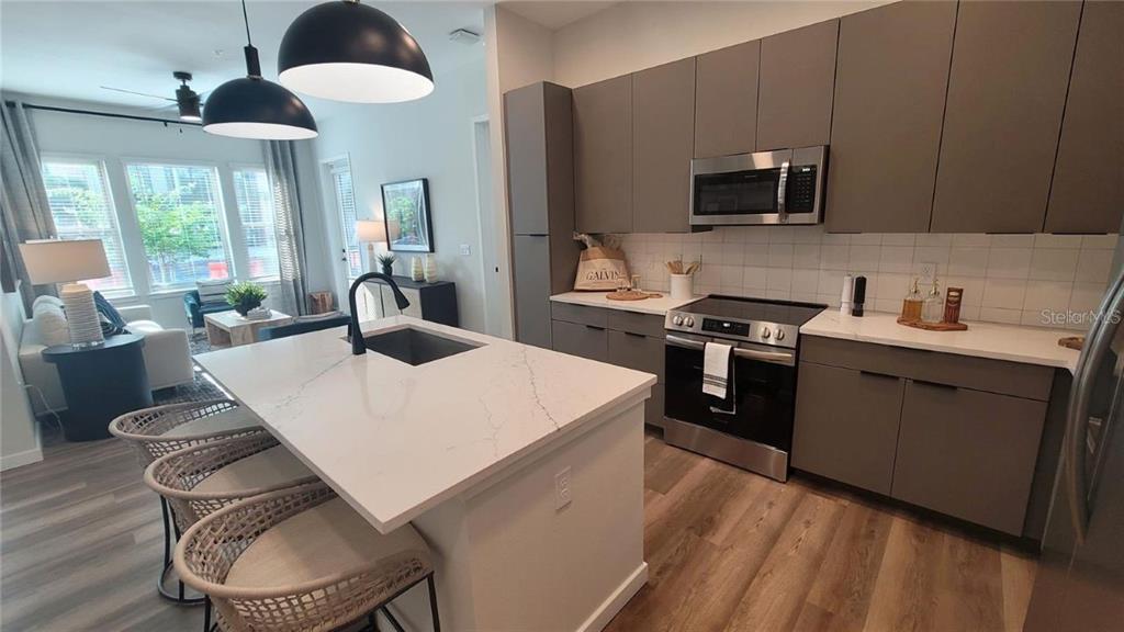 A modern kitchen features gray flat-panel cabinets, a white quartz island, and stainless steel appliances — 10215 ESTUARY LAKES DRIVE UNIT 220, TAMPA, FL