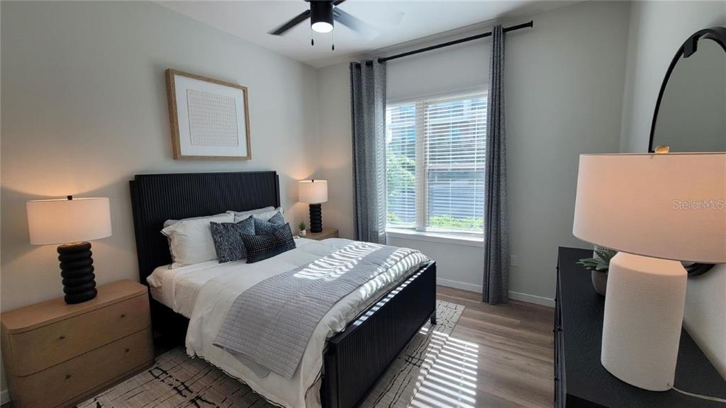 A bedroom features a black bed frame, light wood flooring, and a window with curtains — 10215 ESTUARY LAKES DRIVE UNIT 220, TAMPA, FL