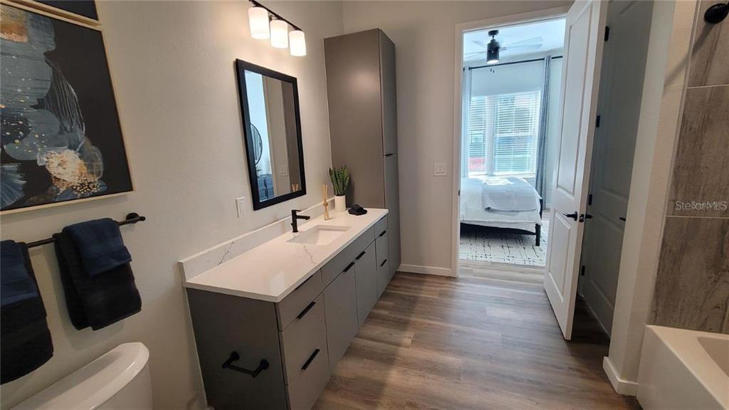 A modern bathroom features a gray vanity, white countertop, and a doorway leading to a bedroom — 10215 ESTUARY LAKES DRIVE UNIT 220, TAMPA, FL