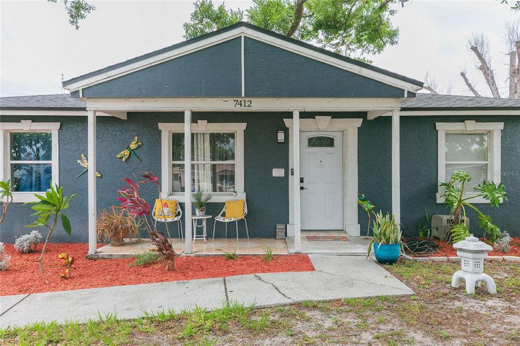 A dark blue house exterior features a covered porch, white trim, and red mulch landscaping — 7412 KINGSTON DRIVE, TAMPA, FL