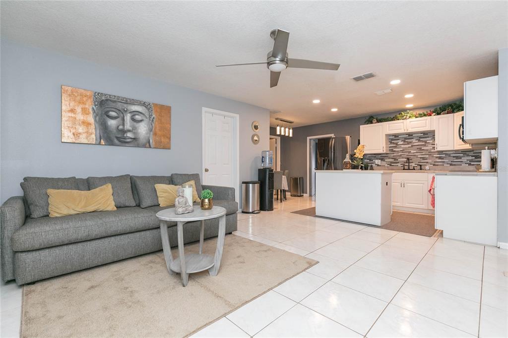 A living room with a gray sofa and a kitchen with white cabinets and tile floors — 7412 KINGSTON DRIVE, TAMPA, FL