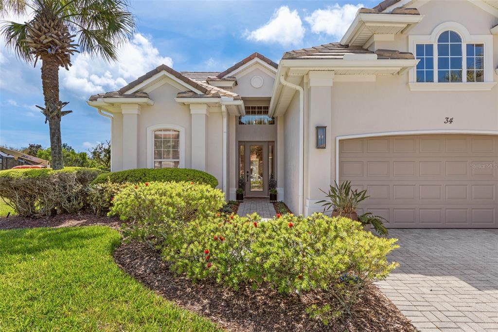 A single-story house with a beige stucco exterior, a paved driveway, and a front garden — 34 SANDPIPER LANE, PALM COAST, FL